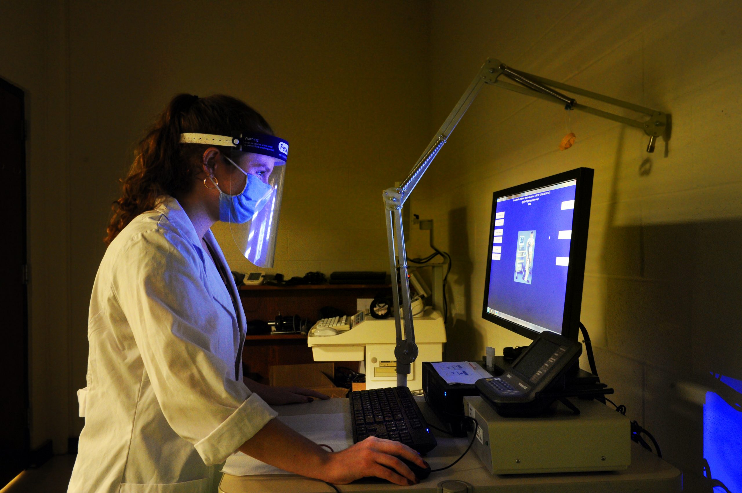 Undergraduate Alyson Nelson is in a white lab coat with a protective face shield doing research on metabolism and body composition. (photo by Donn Young)